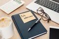 Pen on notebook with job view lettering on sticky note on wooden table with gadgets and cup of coffee.