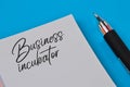 Pen and notebook written with text BUSINESS INCUBATOR
