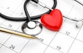 Pen pointing on calendar with stethoscope and red heart. Date for medical examiner