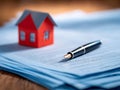 Pen resting on a stack of legal documents with a small red house model in the background symbolizing real estate contract or Royalty Free Stock Photo