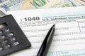 Pen on 1040 US individual income tax filling form with black calculator and US dollar bill, tax submission or revenue calculation