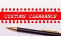 Pen and white torn paper strip on a bright red background with the text CUSTOMS CLEARANCE Royalty Free Stock Photo