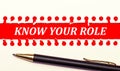 Pen and white torn paper strip on a bright red background with the text KNOW YOUR ROLE Royalty Free Stock Photo