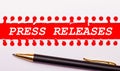 Pen and white torn paper strip on a bright red background with the text PRESS RELEASES