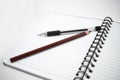 Pencil of brown color and a black color pen placed on top of a white diary