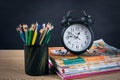 Pencil holder full of colorful pencils with books and black vintage alarm clock on a wooden table
