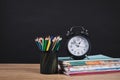 Pencil holder full of colorful pencils with books and black vintage alarm clock on a wooden table