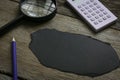 Pencil,magnifying glass and calculator with empty piece of black paper on wooden background. Copy space Royalty Free Stock Photo