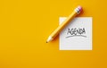 Pencil and a note paper with the word Agenda on yellow background