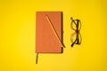 A pencil, orange book and red black glasses on the yellow background Royalty Free Stock Photo