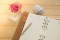 Pencil putting on notebook and pink rose in glass vase on wooden background