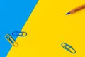 A pencil and three paperclips against a blue and yellow background. Royalty Free Stock Photo