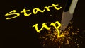 Pencil writing the yellow glowing word startup creating sparks