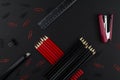 Pencils in black and red, stapler, red and black clips, ruler and knife on a black background