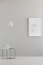 Pendant light above a modern table and a city map poster on a gray wall in a minimalist living room interior and place for a sofa.