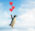 Penguin flying with red heart shaped balloons over water