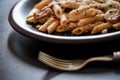 Penne pasta and boscaiola topping sauce in a dish with fork Royalty Free Stock Photo