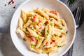 Penne pasta with chicken, pepper and green onions in creamy sauce in a white plate, gray background, top view