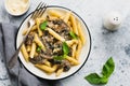 Penne rigate pasta with mushrooms, parmesan cheese and basil leaves in ceramic dish on light old concrete background. Royalty Free Stock Photo