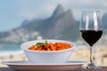 Penne in tomato sauce in a white bowl and a glass of wine with the Ipanema beach in Rio de Janeiro, Brazil in the background Royalty Free Stock Photo