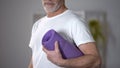 Pensioner holding yoga rug, concept of workouts and healthy lifestyle at old age