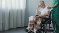 Pensioner sitting in wheelchair, male nurse supporting old patient at clinic Royalty Free Stock Photo