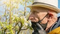 Pensioner smells white tree blossom holding black mask