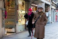 A pensioner with a wand walks along an old narrow street past shop windows