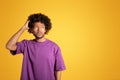 Pensive adult black curly man in purple t-shirt scratching his head, think, look at free space