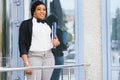 Pensive African American female lawyer in stylish formal suit holding folder with mock up area and looking away standing against Royalty Free Stock Photo