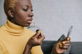 Pensive african american woman applying lip gloss and looking Royalty Free Stock Photo