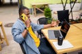 Pensive afro american businessman in stylish clothing talking on mobile phone and using laptop outdoors cafe, drinking Royalty Free Stock Photo