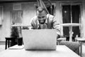 Pensive afro american businessman in stylish clothing talking on mobile phone and using laptop outdoors cafe, drinking Royalty Free Stock Photo