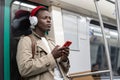 Pensive Black man in subway train thinking using cellphone listens to music with wireless headphones