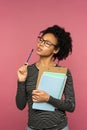 Pensive Afro-American teacher woman isolated on pink studio wall. Student girl wear glasses holding folder, notebooks and pen, Royalty Free Stock Photo