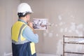 Pensive architect in white helmet looking at picture in hands stands against shabby wall