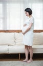 Pensive asian pregnant woman dreaming about child standing near window. Young happy expectant thinking about her baby and enjoying Royalty Free Stock Photo