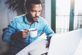 Pensive bearded African man using laptop home while drinking cup black coffee at the wooden table.Concept of young Royalty Free Stock Photo