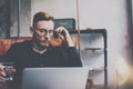 Pensive bearded businessman in eyeglasses working at modern loft.Man sitting in vintage chair,holding in hands glass of Royalty Free Stock Photo