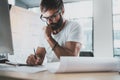 Pensive bearded designer wearing eye glasses and white tshirt, working at modern loft studio-office.Man drawing scetches Royalty Free Stock Photo