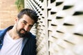 Pensive bearded male leaning on wall with hand on chin