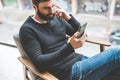 Pensive bearded man sitting home and using mobile smartphone. Man using gadget at hotel lobby. Horizontal. Blurred