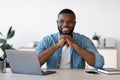 Pensive Black Man Office Worker Sitting At Desk With Laptop And Smiling Royalty Free Stock Photo