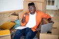 Pensive Black Young Man Sitting Among Cardboard Boxes And Using Laptop Royalty Free Stock Photo