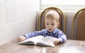 a pensive blond-haired three-year-old boy sitting at the table and reading a book Royalty Free Stock Photo