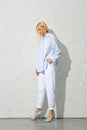 Pensive blonde woman in blue shirt, white jeans and stilettos looking down