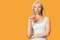 Blonde woman holding pencil near mouth while thinking isolated on orange Royalty Free Stock Photo