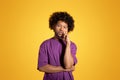 Pensive bored sad mature black curly man in purple t-shirt thinks, chooses isolated on yellow background Royalty Free Stock Photo