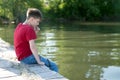 A pensive boy sits on a wooden pier, having lowered his feet in the water, and is nibbling a blade of grass. Royalty Free Stock Photo