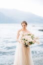 Pensive bride with a bouquet of flowers stands on the shore of Lake Como against a background of mountains Royalty Free Stock Photo